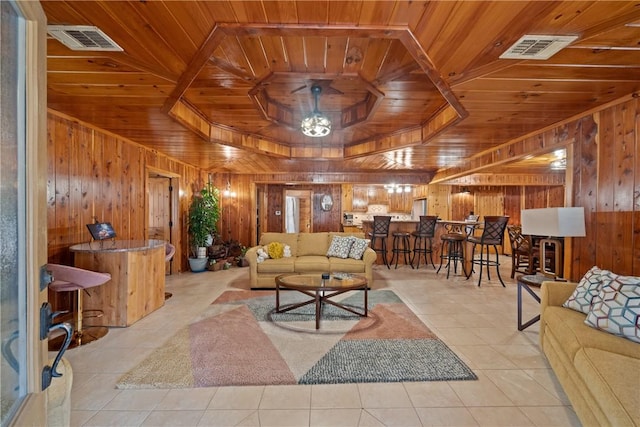 living area featuring visible vents, light tile patterned flooring, wood ceiling, wood walls, and a raised ceiling