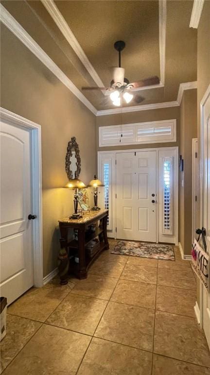 tiled foyer with a raised ceiling, ceiling fan, and ornamental molding