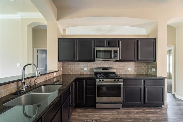kitchen featuring stainless steel appliances, a sink, dark stone countertops, arched walkways, and tasteful backsplash
