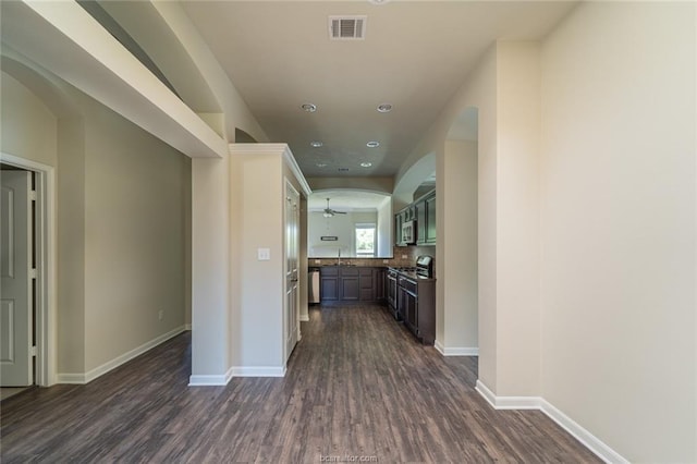 hallway featuring dark wood-style floors, baseboards, recessed lighting, and arched walkways