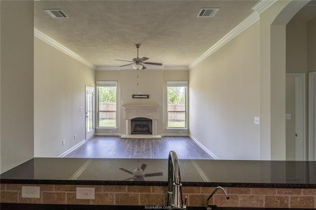 unfurnished living room featuring a ceiling fan, dark wood-style floors, a fireplace with raised hearth, arched walkways, and a textured ceiling