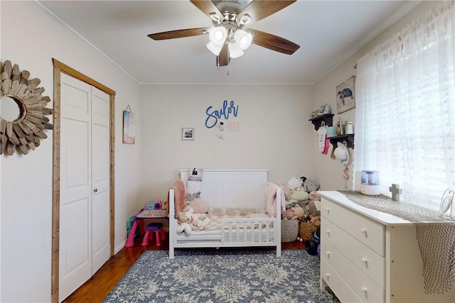 bedroom featuring a crib, dark hardwood / wood-style floors, multiple windows, and ceiling fan