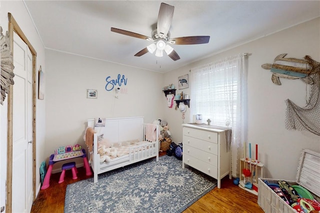 bedroom featuring a crib, hardwood / wood-style floors, and ceiling fan