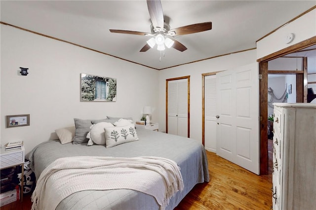 bedroom with ceiling fan, two closets, and light hardwood / wood-style flooring