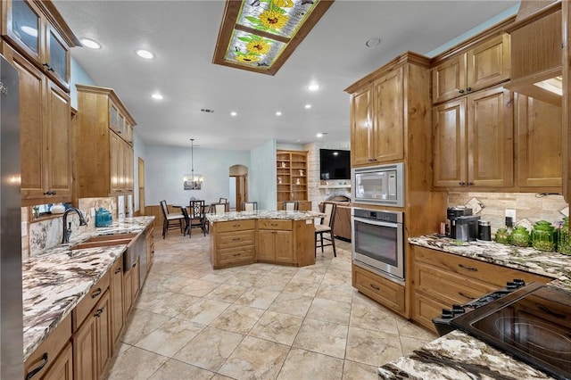 kitchen featuring light stone counters, decorative light fixtures, stainless steel appliances, a kitchen island, and sink