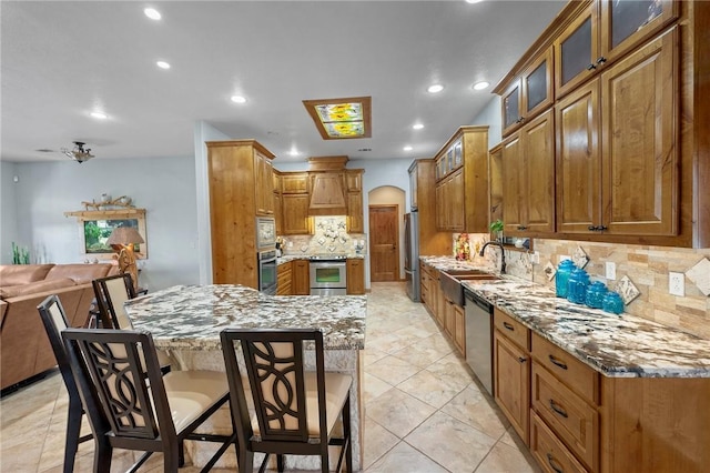 kitchen featuring stainless steel appliances, sink, a breakfast bar area, backsplash, and light stone countertops