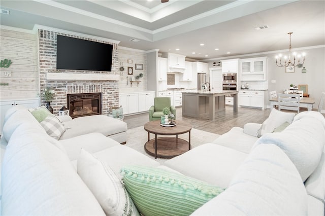 living room featuring wooden walls, crown molding, an inviting chandelier, a fireplace, and light hardwood / wood-style floors