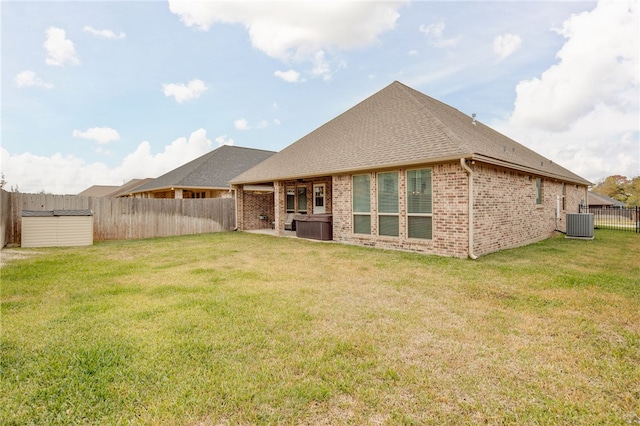 rear view of house with a hot tub, central AC, and a lawn