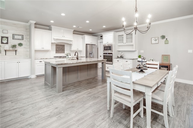 kitchen featuring a center island with sink, light stone countertops, appliances with stainless steel finishes, decorative light fixtures, and white cabinetry