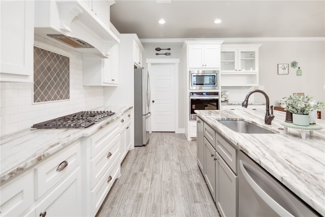 kitchen featuring ornamental molding, stainless steel appliances, sink, white cabinets, and light hardwood / wood-style floors