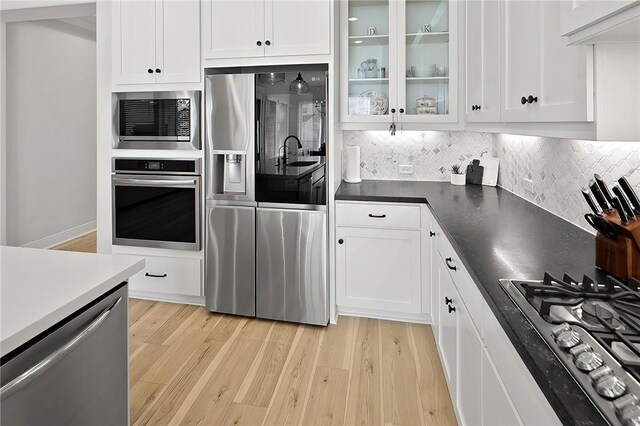 3609 Llano River Dr, College Station, TX 77845 - kitchen featuring appliances with stainless steel finishes, light wood-style flooring, white cabinetry, backsplash, and glass insert cabinets
