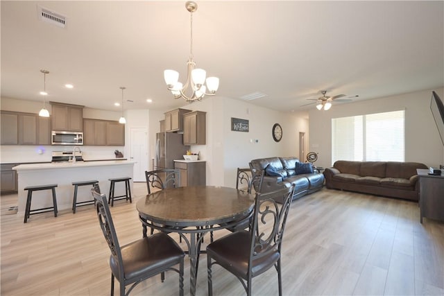 dining room featuring light wood-type flooring, ceiling fan with notable chandelier, and sink