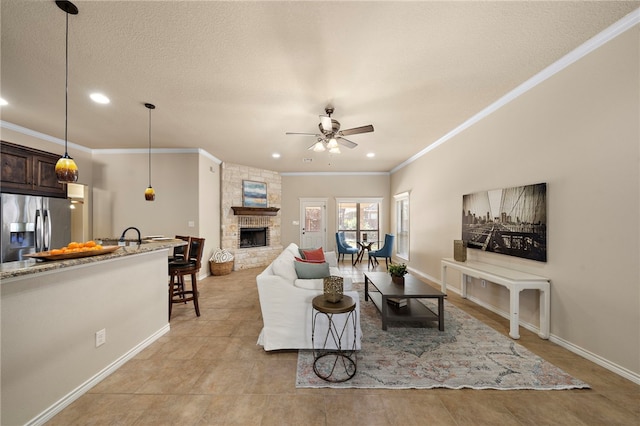 living room featuring a textured ceiling, ceiling fan, ornamental molding, and a stone fireplace