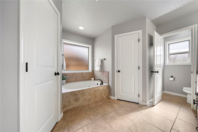 bathroom with a textured ceiling, tiled tub, tile patterned floors, and toilet