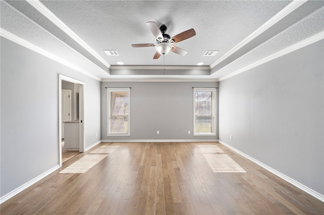 empty room featuring a raised ceiling, crown molding, and light hardwood / wood-style flooring