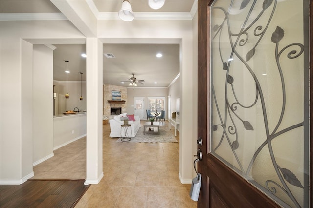 foyer entrance featuring light tile patterned flooring, ceiling fan, crown molding, and a stone fireplace