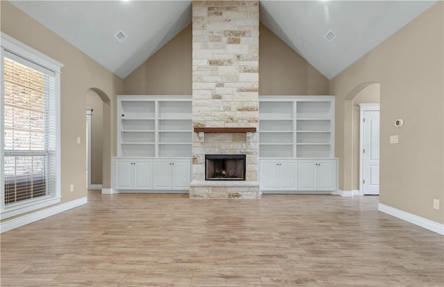 3520 Foxcroft Path, Bryan, TX 77808 - unfurnished living room featuring arched walkways, high vaulted ceiling, light wood-type flooring, a stone fireplace, and baseboards