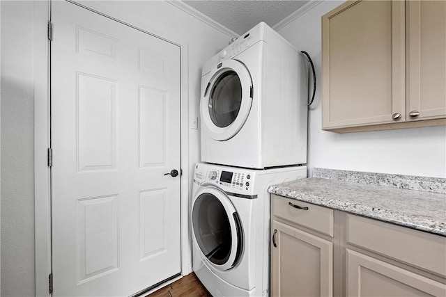 laundry area with cabinets, stacked washer and clothes dryer, dark hardwood / wood-style floors, ornamental molding, and a textured ceiling