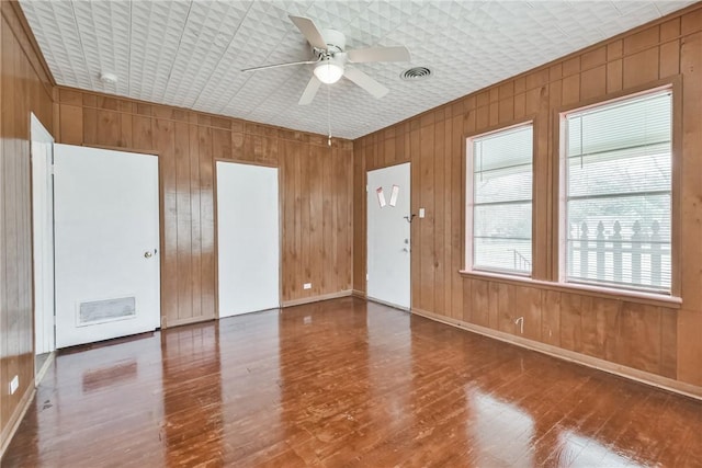 empty room featuring wood-type flooring, ceiling fan, and wood walls