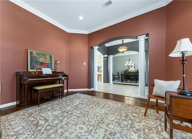 living area with arched walkways, a notable chandelier, visible vents, wood finished floors, and ornate columns