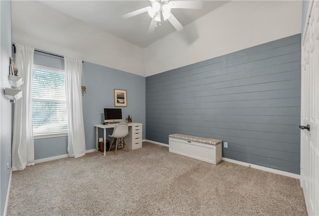 carpeted home office with wood walls, baseboards, and a ceiling fan