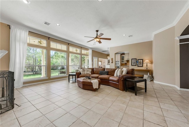 living area featuring light tile patterned floors, visible vents, baseboards, ceiling fan, and ornamental molding