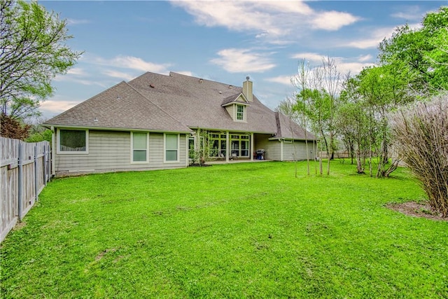 back of house featuring a fenced backyard, a lawn, a chimney, and roof with shingles