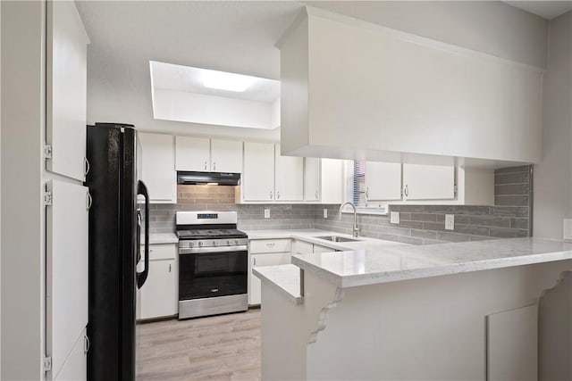 kitchen with sink, stainless steel gas stove, white cabinetry, black fridge, and kitchen peninsula