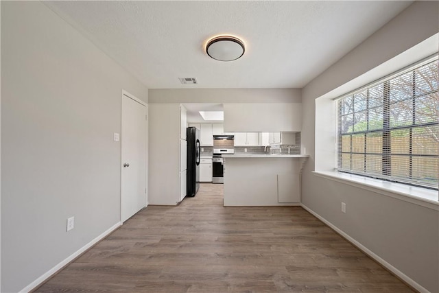 kitchen with white cabinetry, kitchen peninsula, black fridge, stainless steel range oven, and light hardwood / wood-style flooring