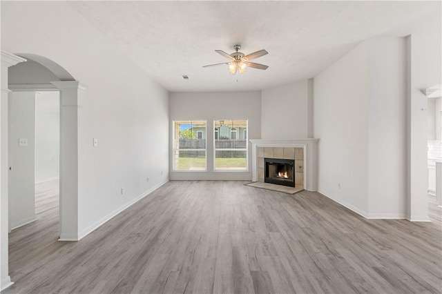 unfurnished living room with ceiling fan, a tiled fireplace, ornate columns, and light hardwood / wood-style flooring