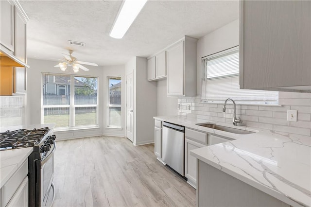 kitchen with light stone countertops, sink, stainless steel appliances, decorative backsplash, and light wood-type flooring