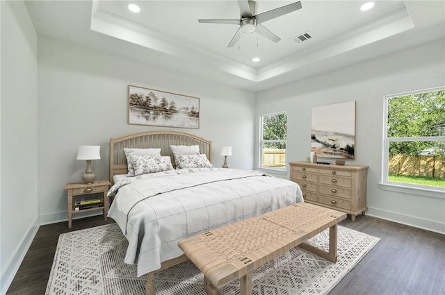 bedroom with dark hardwood / wood-style floors, ceiling fan, and a raised ceiling