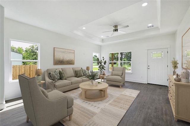 living room featuring ceiling fan, a raised ceiling, and dark wood-type flooring