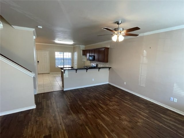 kitchen featuring a breakfast bar area, dark hardwood / wood-style flooring, ornamental molding, ceiling fan, and kitchen peninsula