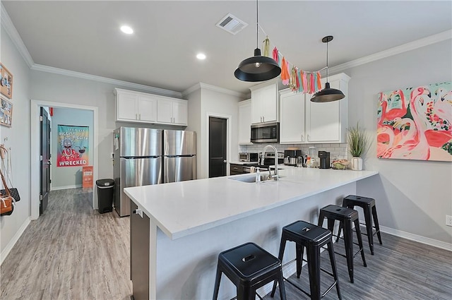 303 Luther St, College Station, TX 77840 - kitchen featuring stainless steel appliances, a peninsula, light wood-style flooring, ornamental molding, and a kitchen bar