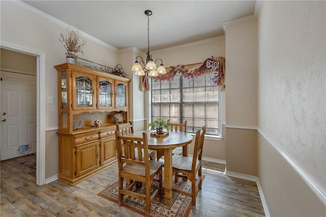 dining area with light wood-type flooring, ornamental molding, and an inviting chandelier