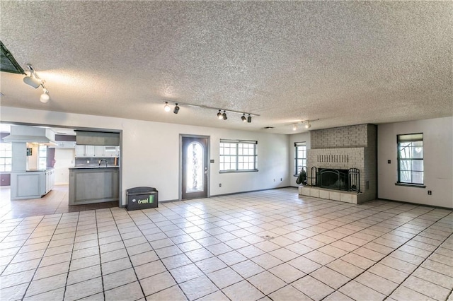 180 Fcr 797, Donie, TX 75838 - unfurnished living room with track lighting, light tile patterned floors, a brick fireplace, a textured ceiling, and a sink