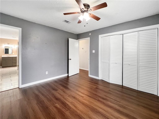 unfurnished bedroom featuring ceiling fan, ensuite bathroom, and dark wood-type flooring