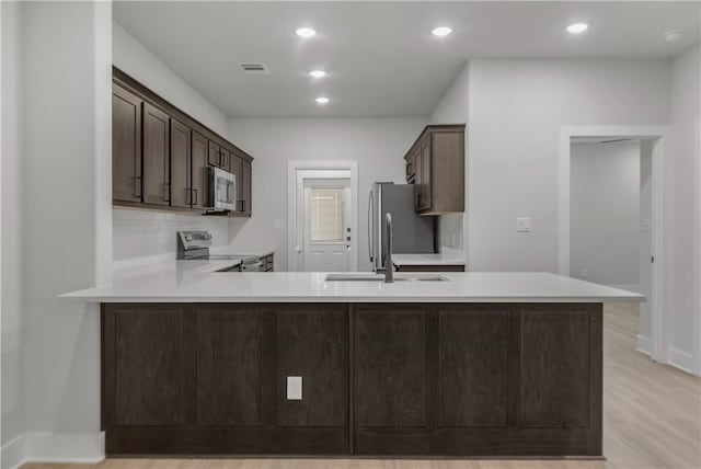 kitchen featuring sink, light hardwood / wood-style flooring, kitchen peninsula, and appliances with stainless steel finishes