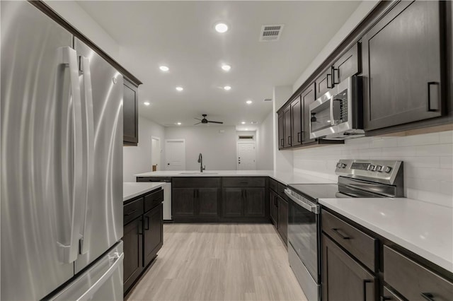 kitchen featuring sink, light hardwood / wood-style flooring, dark brown cabinets, stainless steel appliances, and decorative backsplash