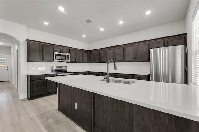 kitchen featuring sink, dark brown cabinets, light hardwood / wood-style flooring, stainless steel appliances, and backsplash