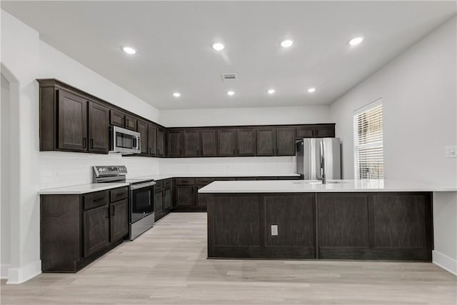 kitchen featuring sink, decorative backsplash, dark brown cabinetry, stainless steel appliances, and light hardwood / wood-style flooring