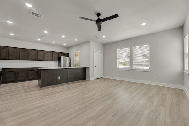 kitchen with dark brown cabinetry, light wood-type flooring, stainless steel refrigerator, an island with sink, and ceiling fan