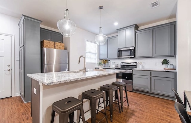 kitchen with a kitchen island with sink, decorative light fixtures, stainless steel appliances, and a kitchen bar