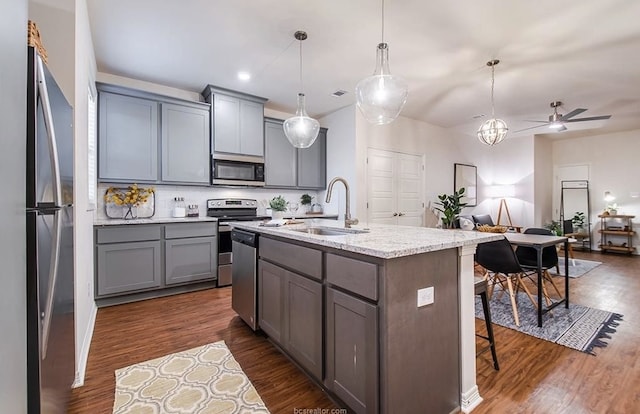 kitchen featuring appliances with stainless steel finishes, pendant lighting, sink, a kitchen island with sink, and light stone countertops