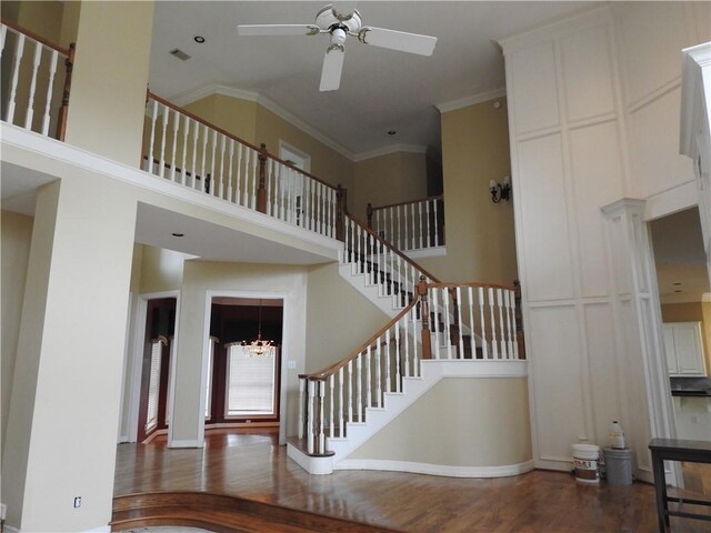 staircase featuring hardwood / wood-style floors, ceiling fan with notable chandelier, a towering ceiling, and ornamental molding