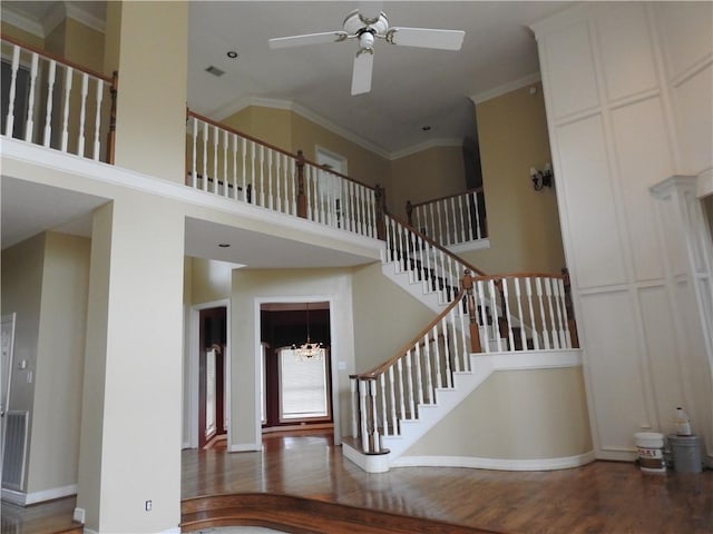 stairs with ceiling fan with notable chandelier, wood-type flooring, a towering ceiling, and ornamental molding