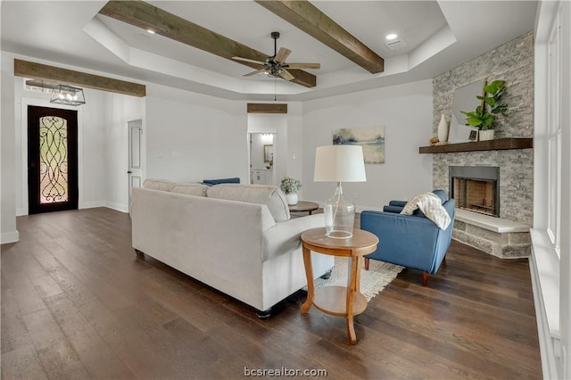 living room featuring dark wood-type flooring, a raised ceiling, ceiling fan, a fireplace, and beam ceiling