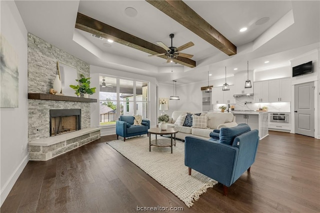 living room with dark hardwood / wood-style floors, ceiling fan, a stone fireplace, and beam ceiling