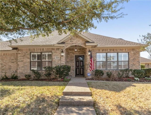 ranch-style home with a front yard, brick siding, and roof with shingles